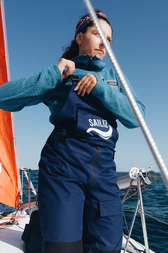 La salopette pour la voile qui s'adapte aux navigatrices. Photo d'une femme en train d'ajuster sa salopette de voile sur un bateau. 