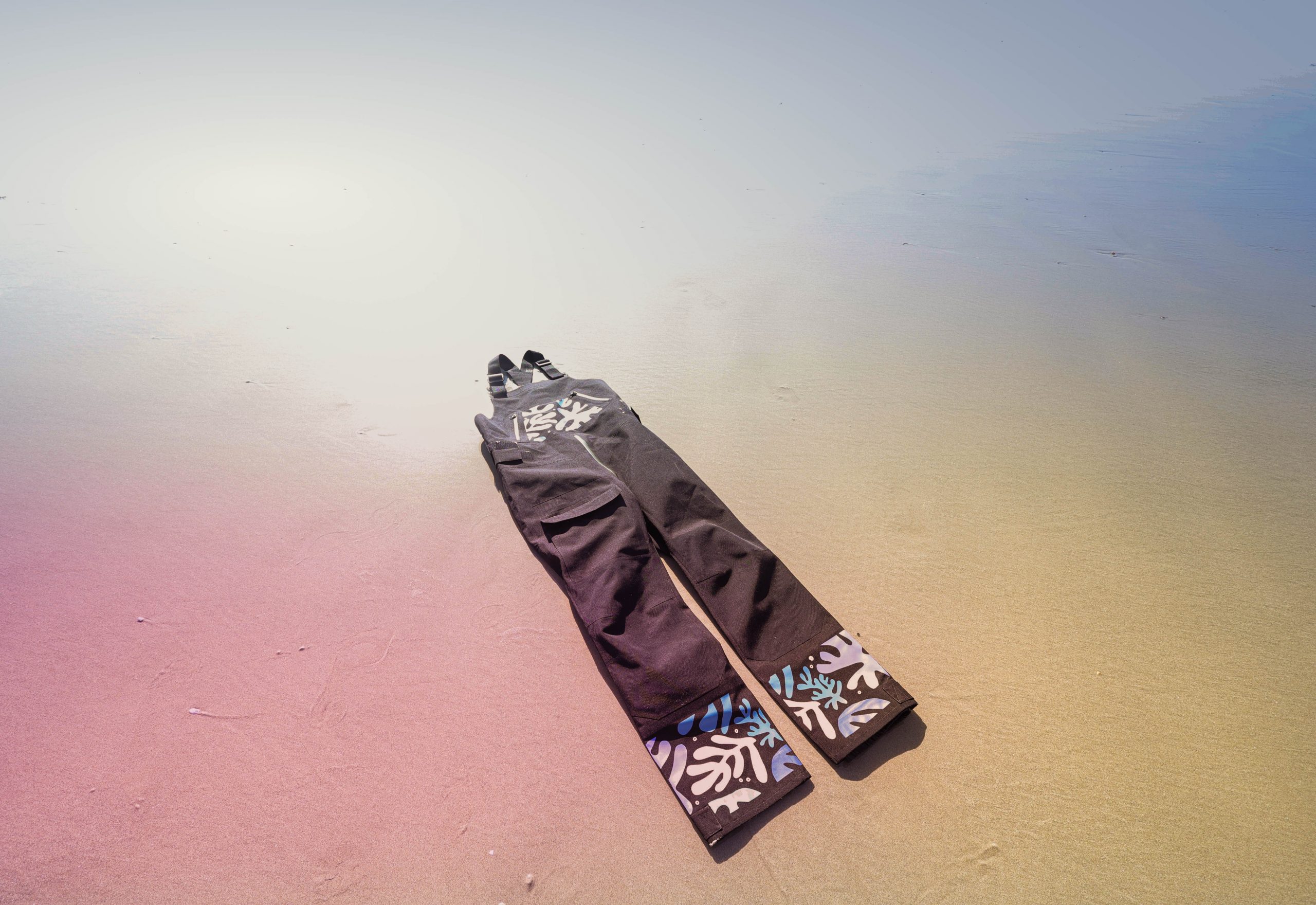 Salopette pour la voile posée sur du sable avec des motifs organiques sur une plage bretonne. 